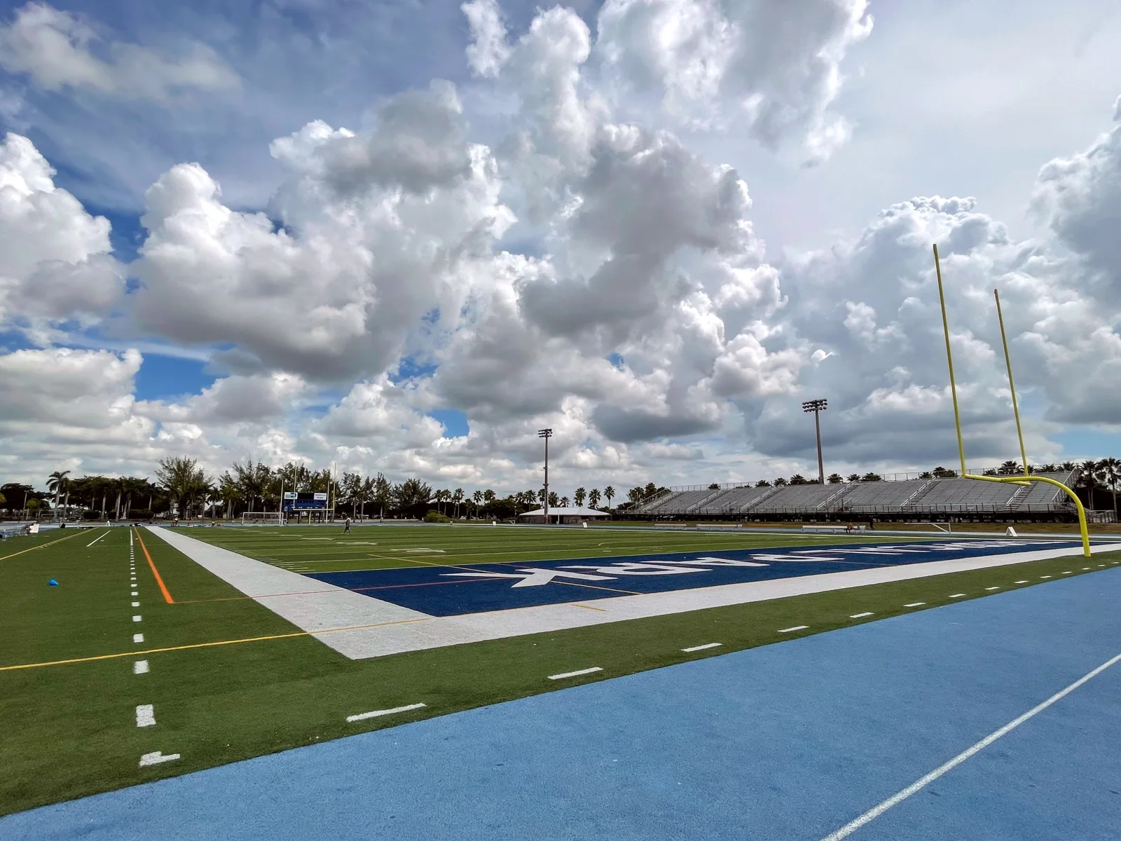 Football field, goalposts, and empty bleachers at Tropical Park Stadium under a cloudy Miami sky